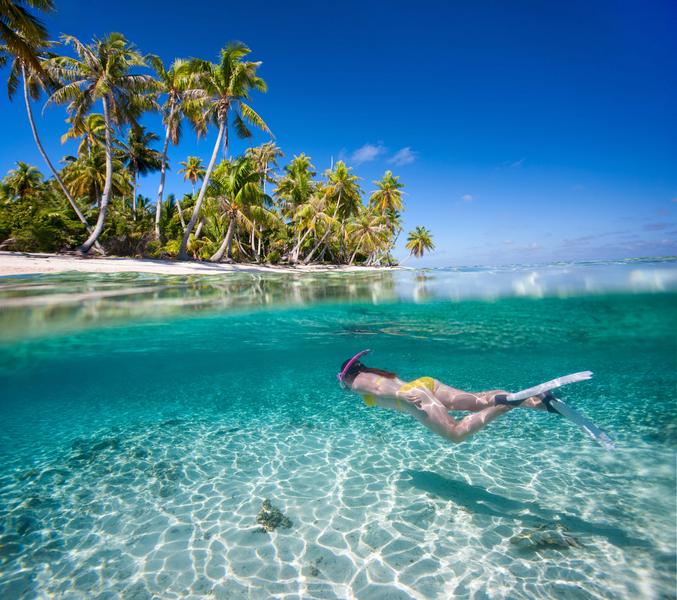 Woman swimming underwater in clear tropical waters in front of exotic island, French Polynesia