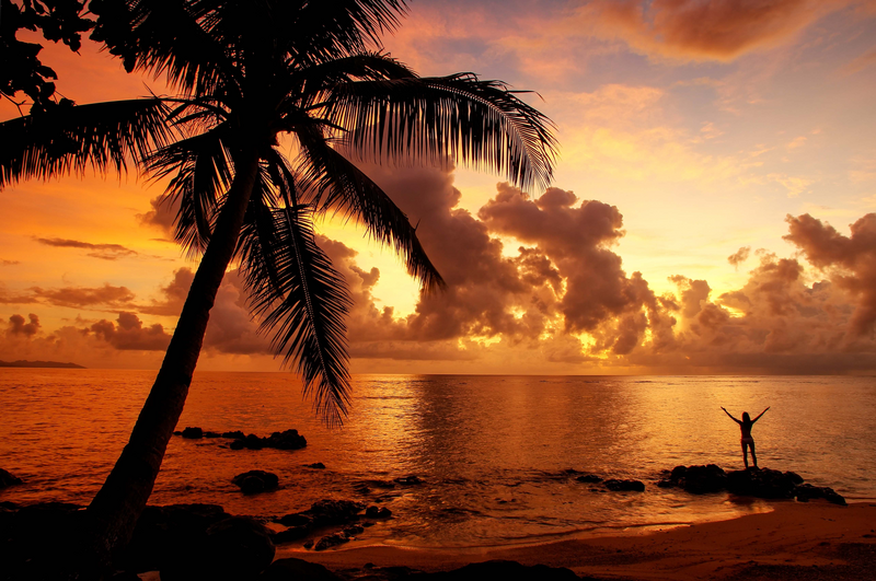 A traveler enjoys a colorful sunrise on the beach in Lavena village on Taveuni Island, Fiji