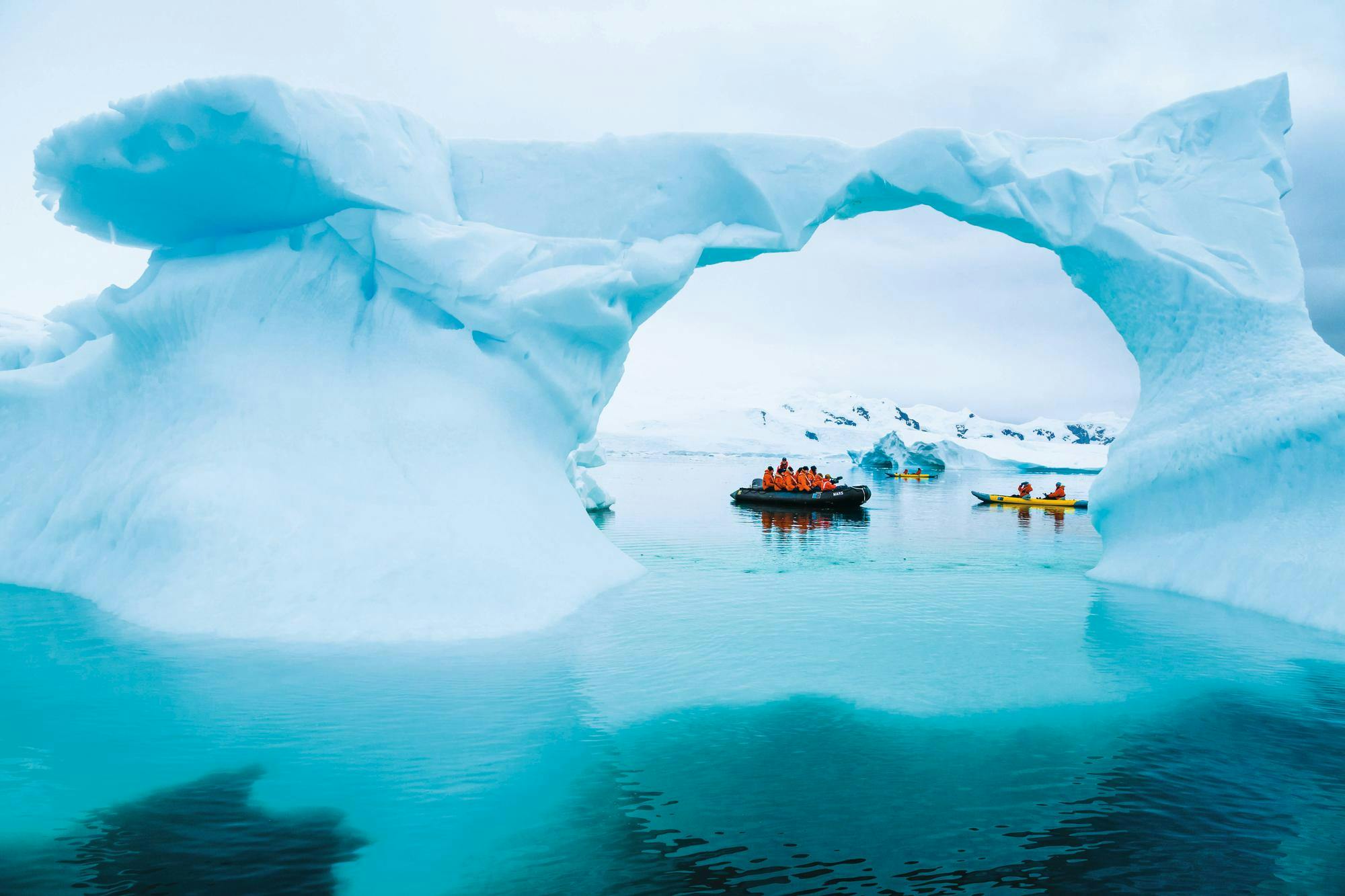 Guests exploring by zodiac and kayaks see a blue ice arch/blue iceberg up close, at Niko Harbor, Antarctic Peninsula, Southern Ocean, Antarctica.