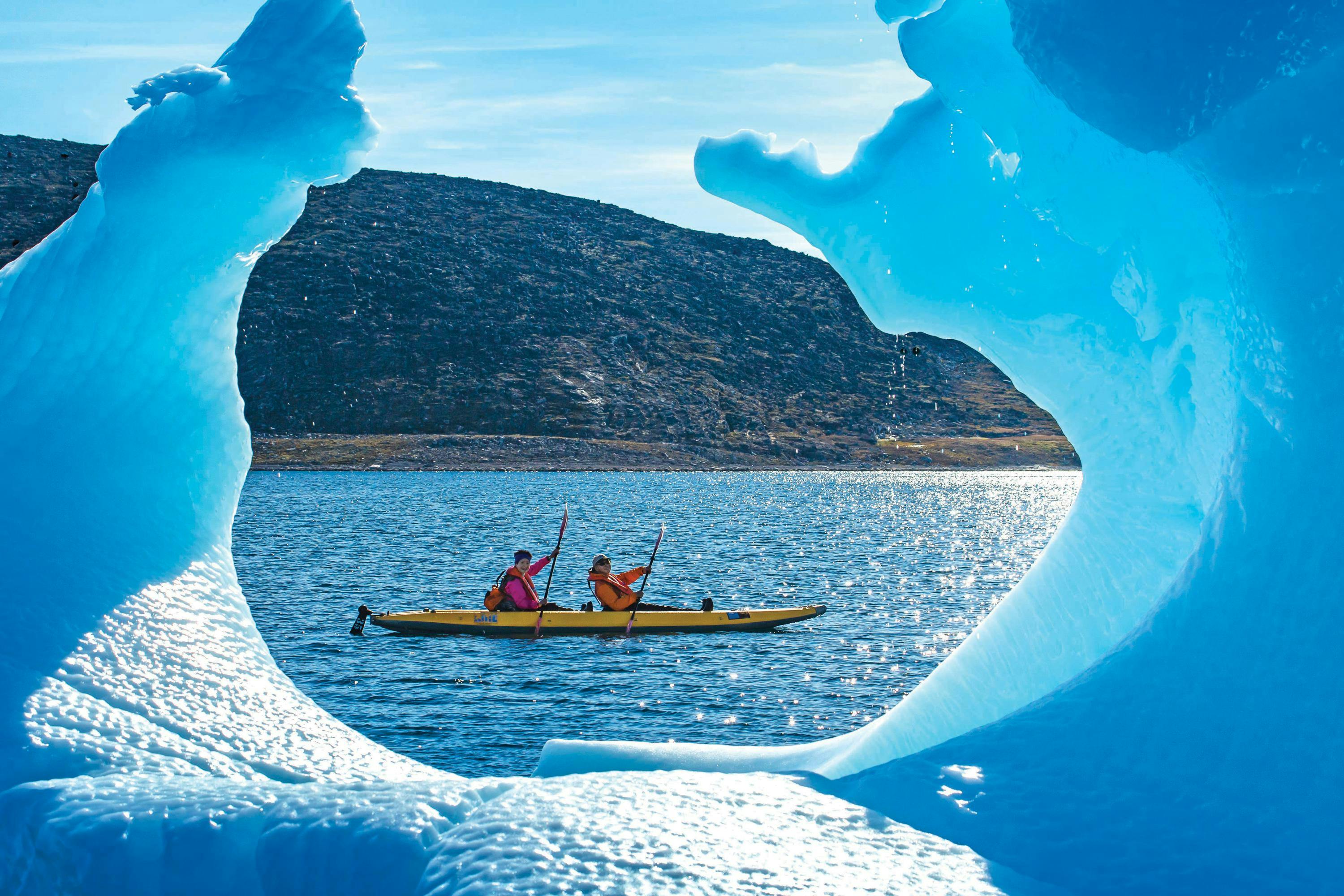 Guests exploring by kayak are framed by an Iceberg in Arctic Harbour, Baffin Bay, Baffin Island, Nunavut, Canada