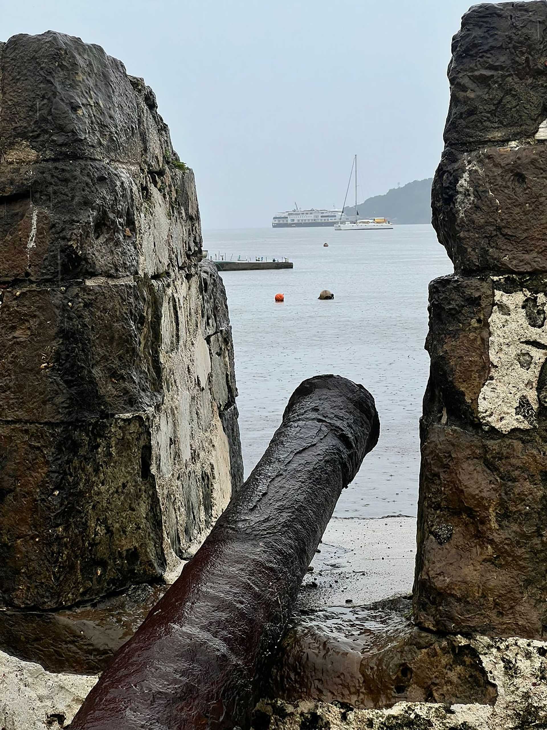 a cannon in a fort wall with sailboats in the background