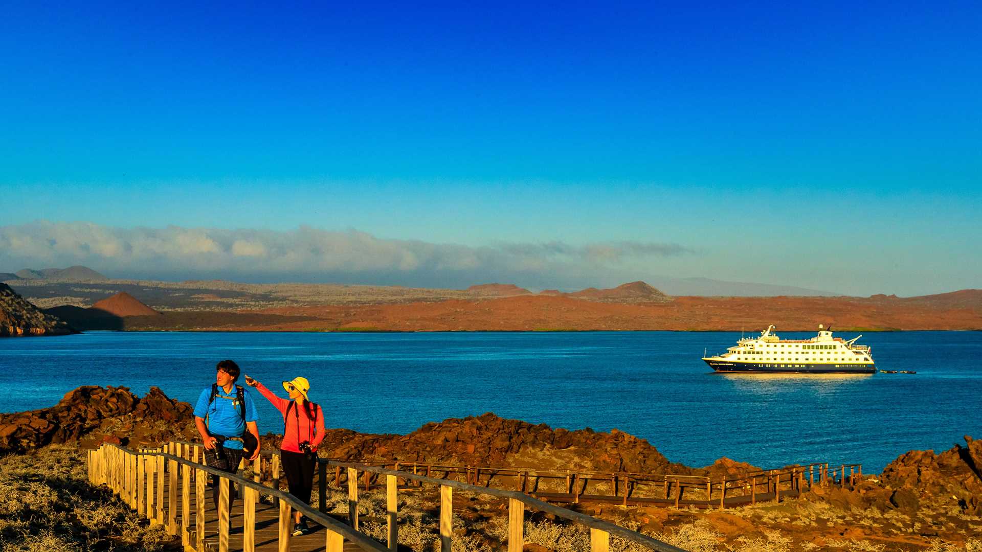 Guests hiking on Bartolome Island, Galápagos with the ship National Geographic Endeavour II in the background.