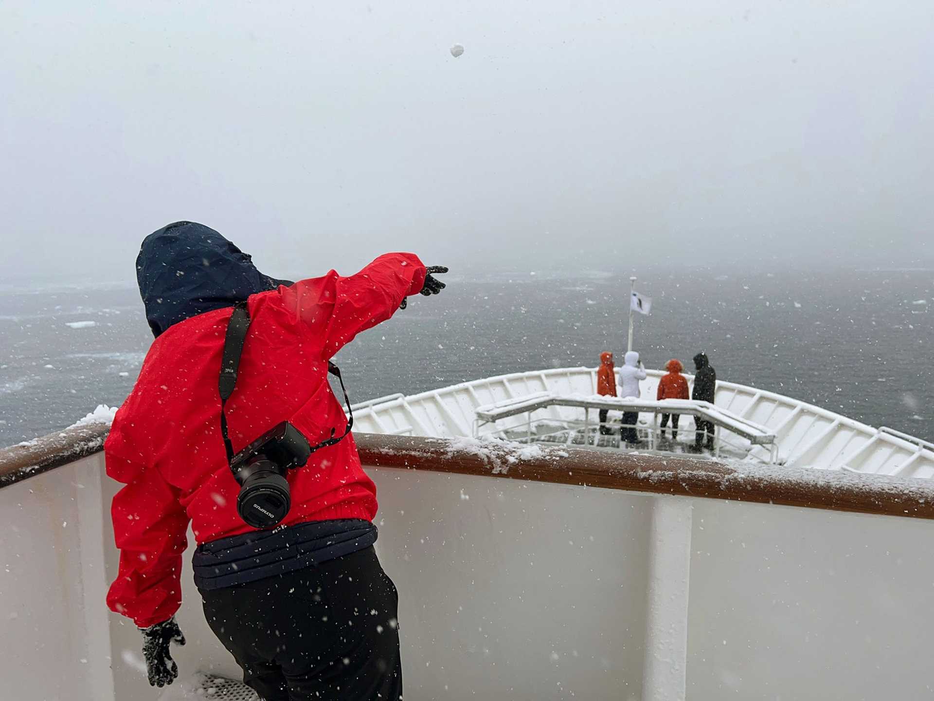 person in a red parka throwing a snowball off the top deck of a ship
