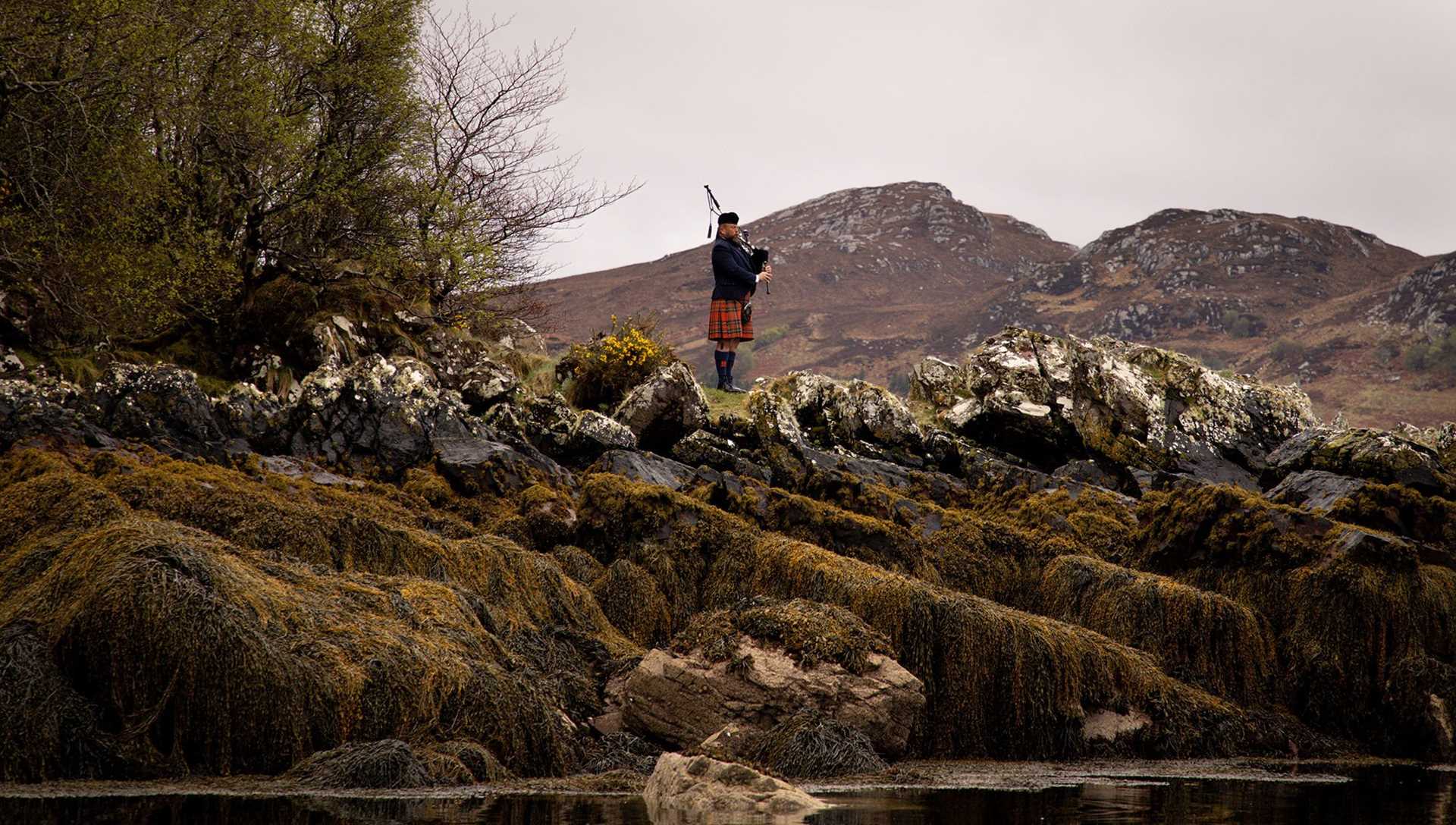 a man playing bagpipes standing on a seaside cliff