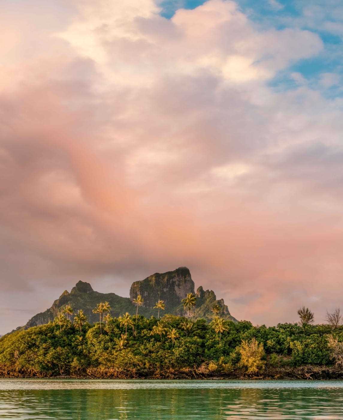 Pink clouds frame a bare hilltop surrounded by lush greenery