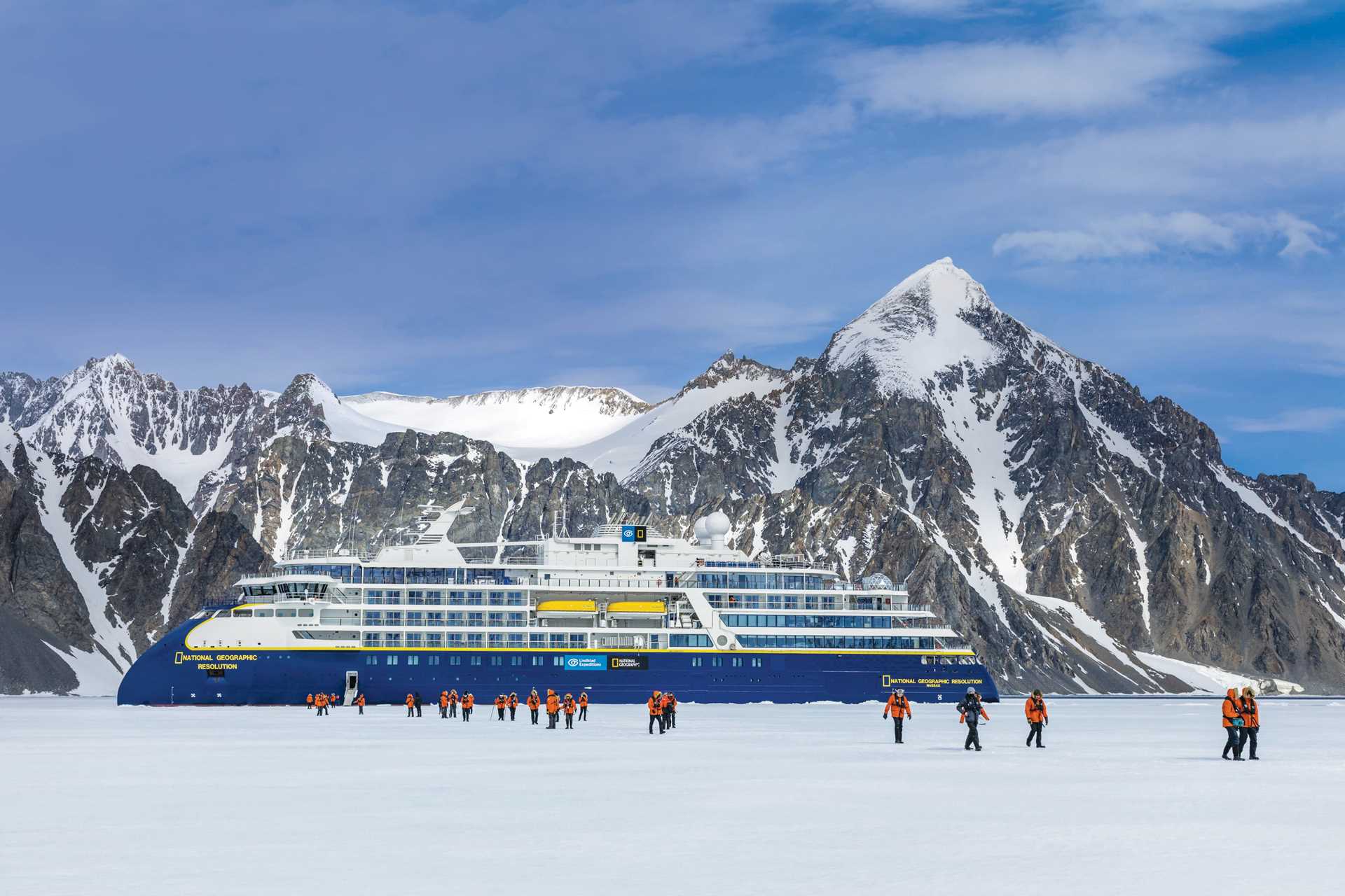 Guests in a Zodiac in the distance cruise under a large iceberg arc off Booth Island.