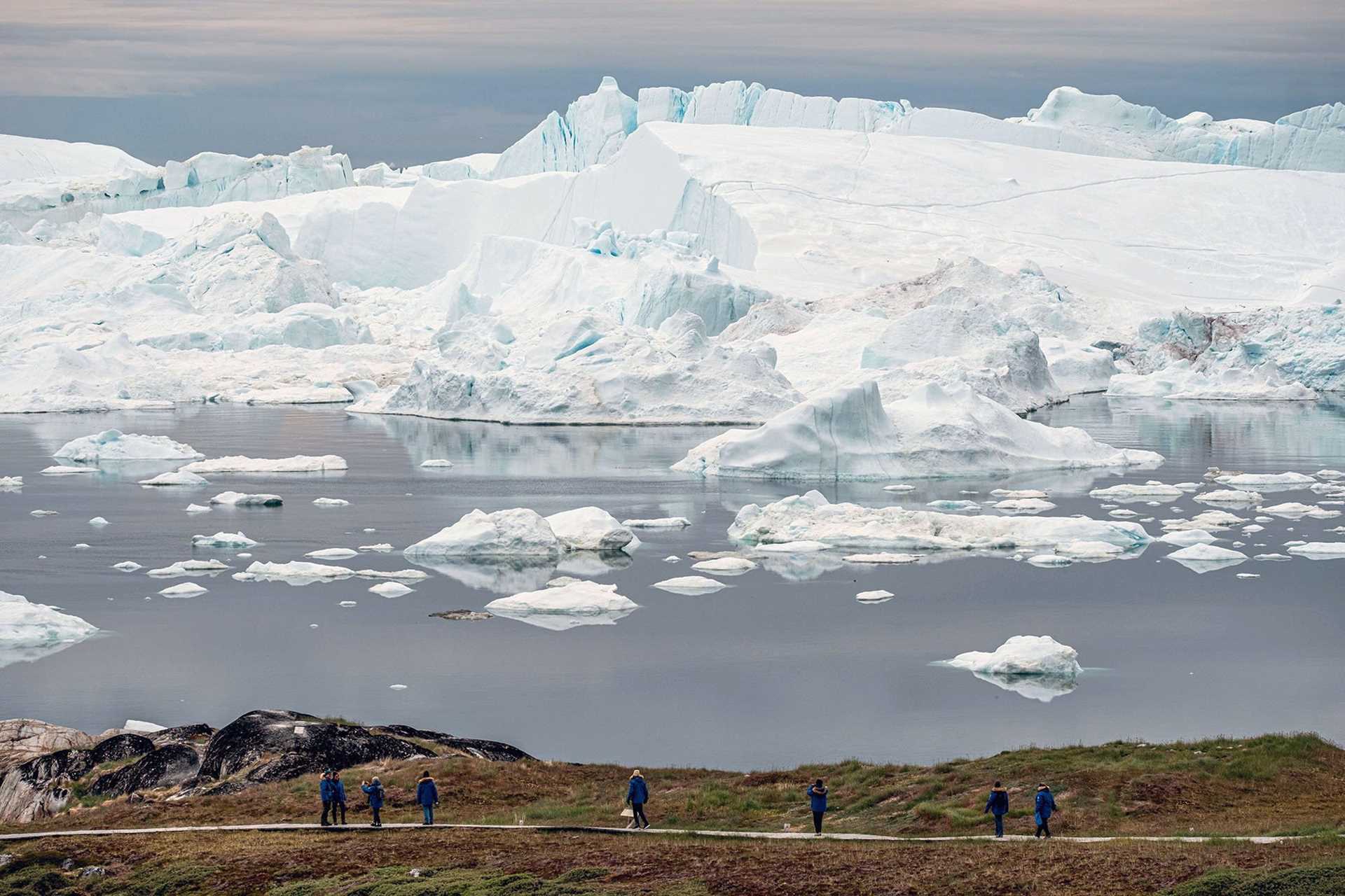 hikers walk with icebergs in the background