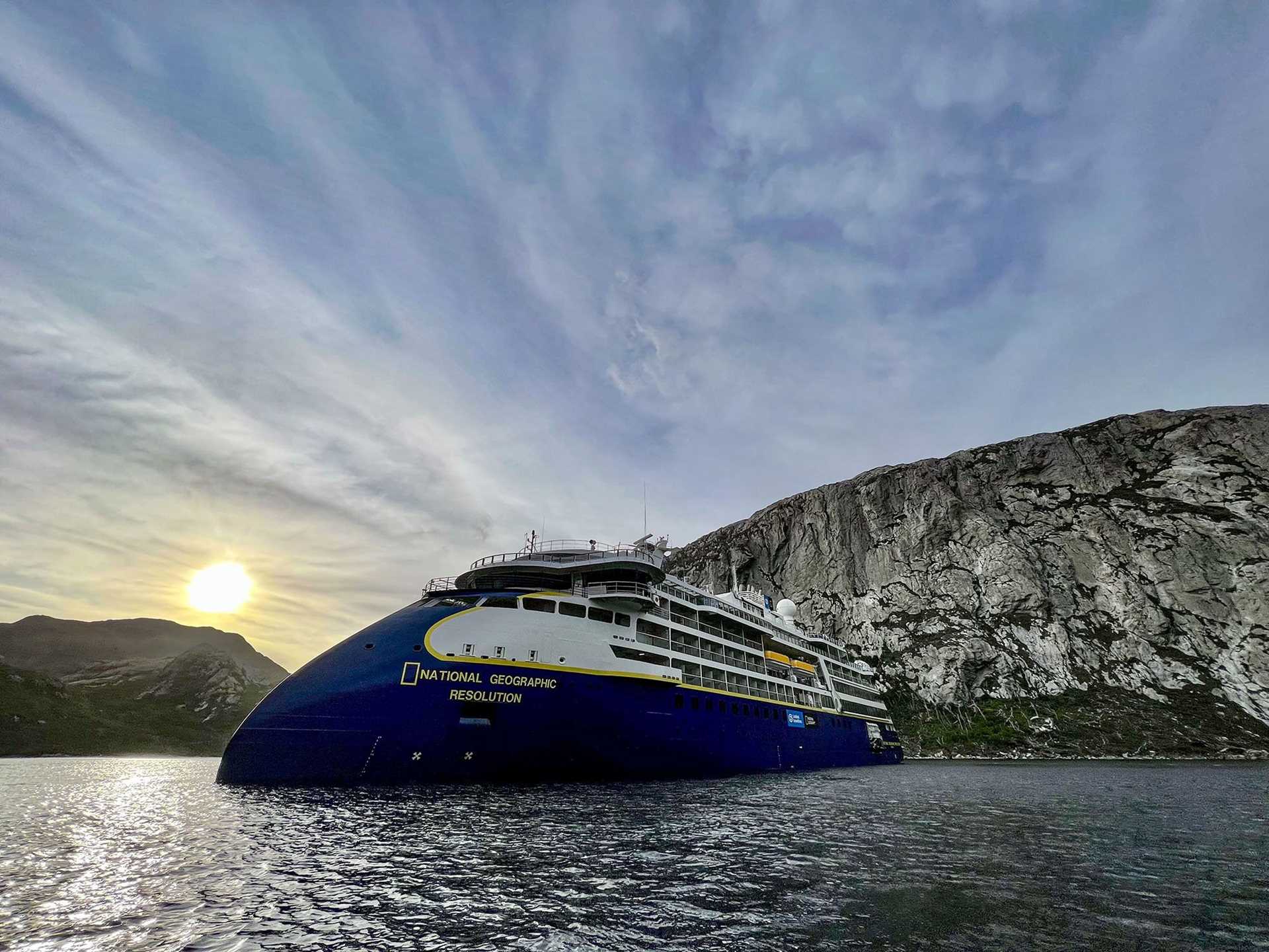 National Geographic Resolution ship in front of hillside with sun shining in background