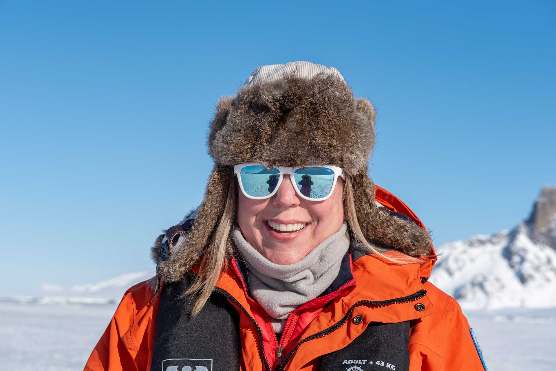 A woman in an orange parka wearing sunglasses