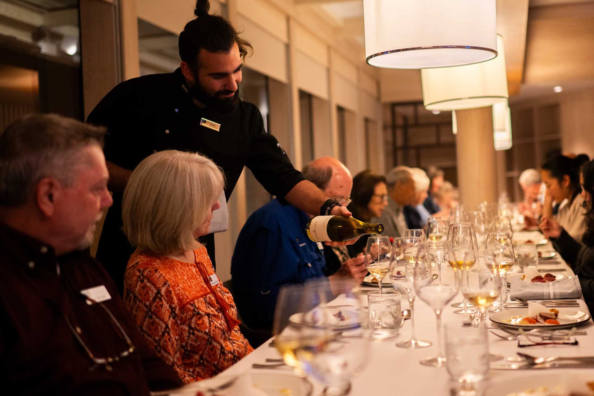 A waiter pours a glass of wine for a woman at a long dining table on the National Geographic Resolution.